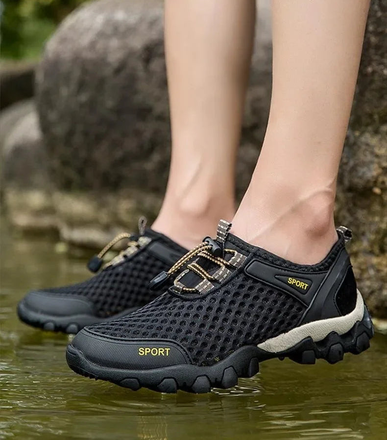Black mesh shoes worn by a person standing in water with rocks in the background