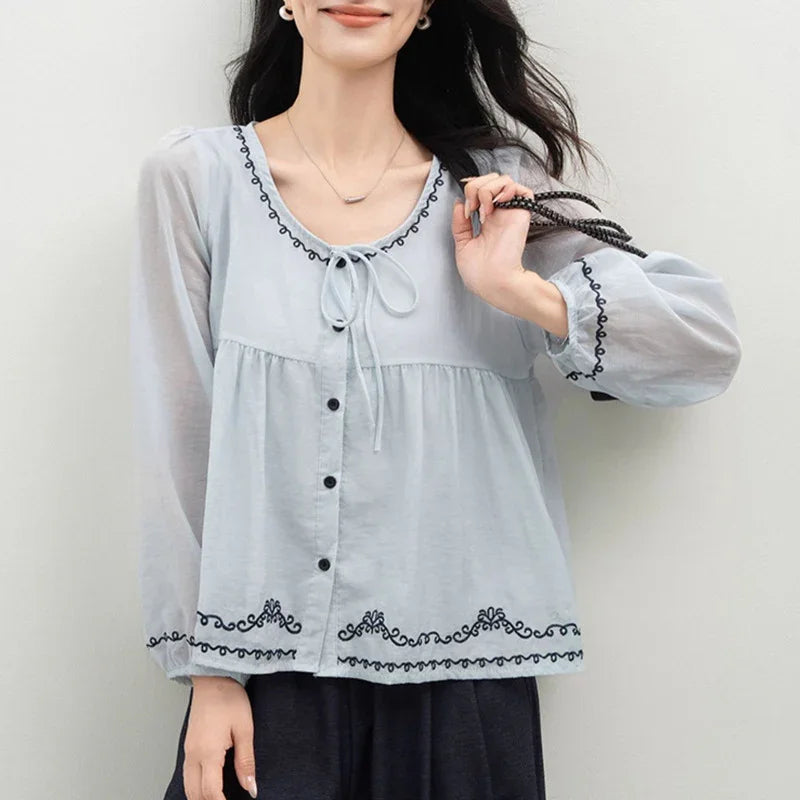 Woman wearing a light blue long-sleeve blouse with black embroidery and front buttons