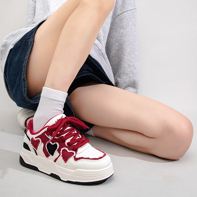 Person wearing red and white sneakers with heart designs, sitting on a light gray background.
