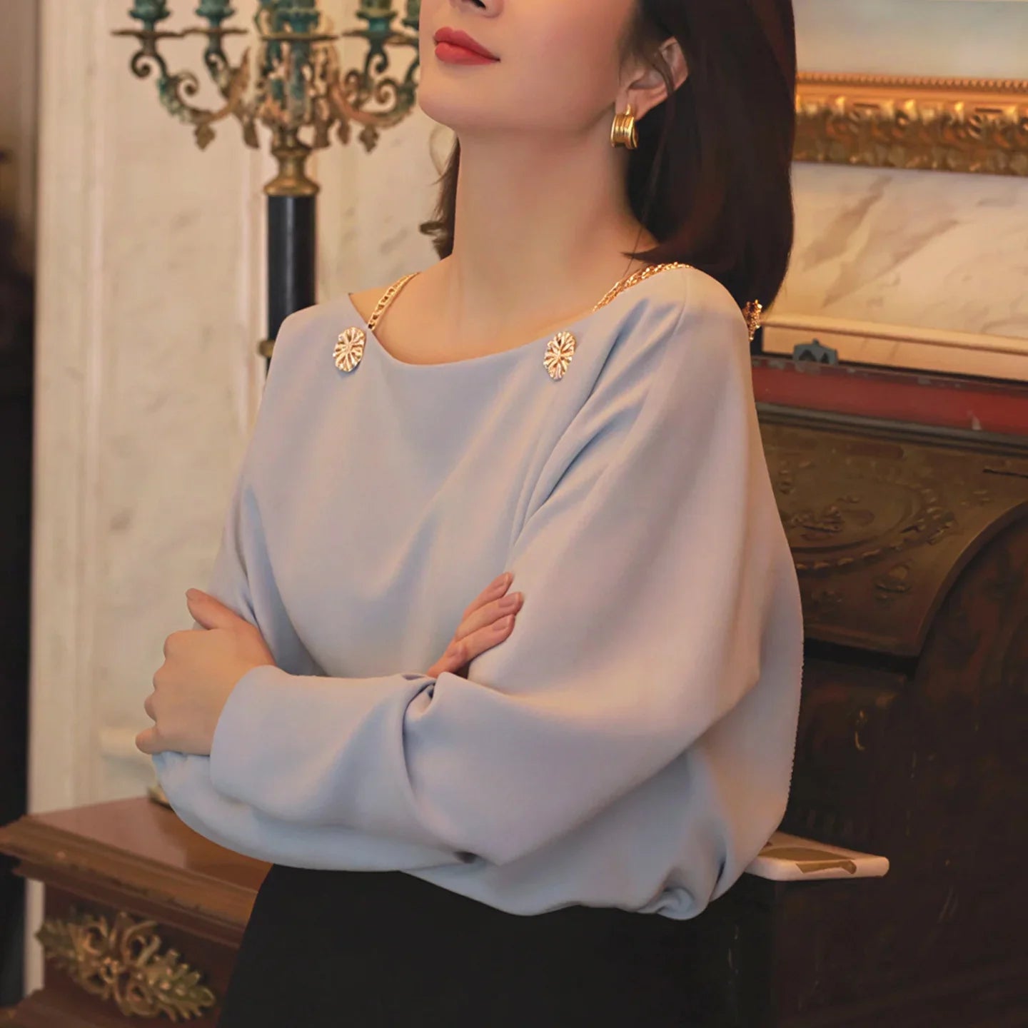 Woman wearing light blue blouse with gold chain straps and floral embellishments, elegant style