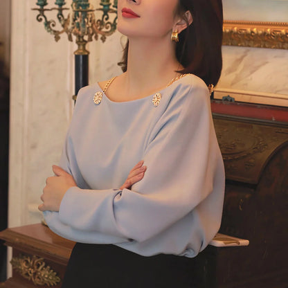 Woman wearing light blue blouse with gold chain straps and floral embellishments, elegant style