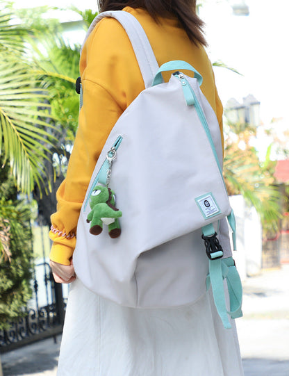 Person wearing a white backpack with a green plush toy attached, outdoors.