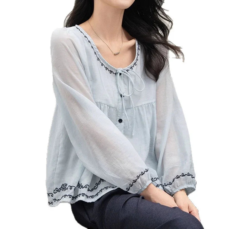Light blue long sleeve blouse with black embroidery, flowy fit, worn by woman