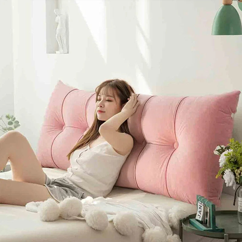 Woman relaxing on a bed with a large pink backrest pillow in a bright bedroom