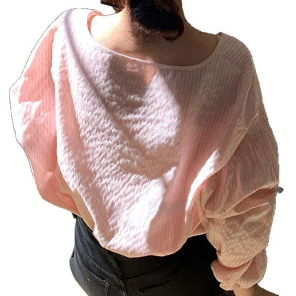 Back view of woman wearing loose light pink textured blouse with puff sleeves and black pants