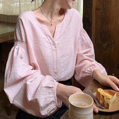 Woman in light pink striped blouse sitting at wooden table with coffee and cheesecake