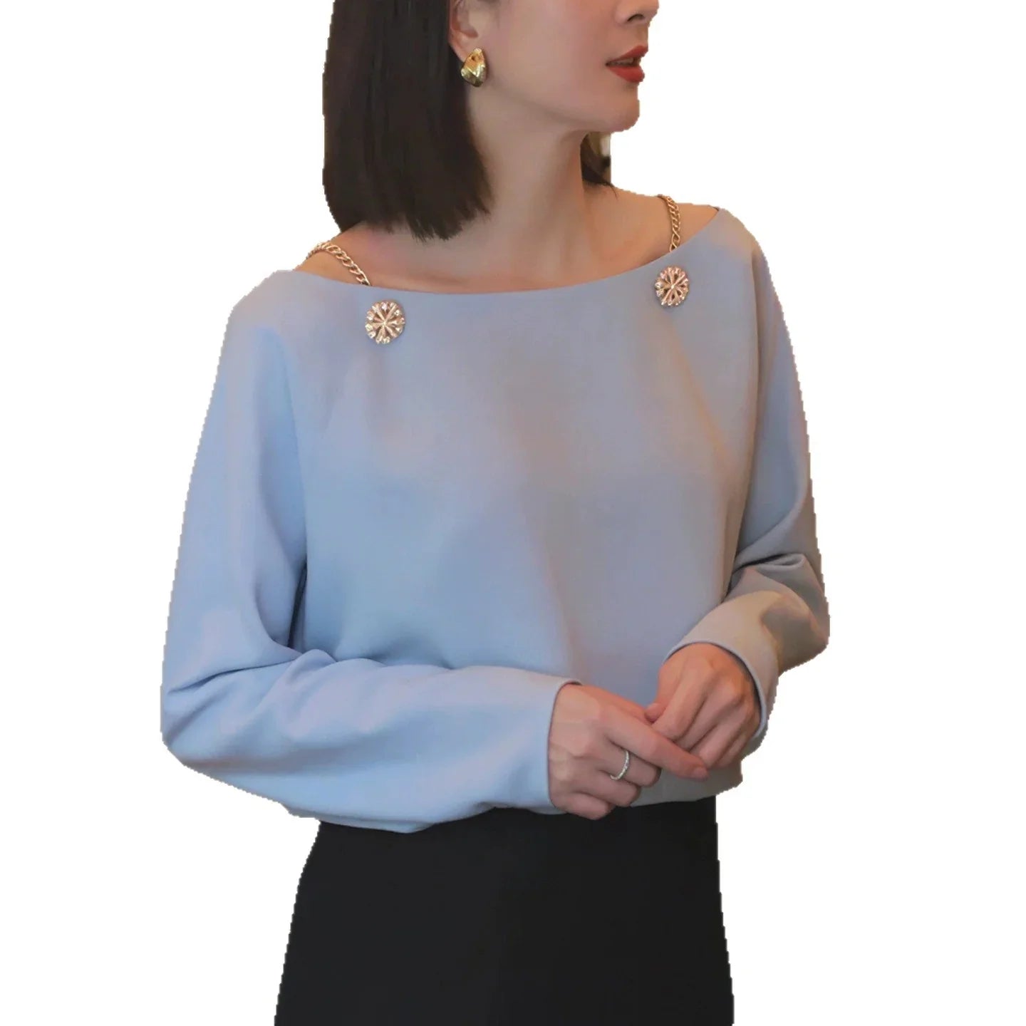 Woman wearing light blue long sleeve blouse with gold chain details and black skirt