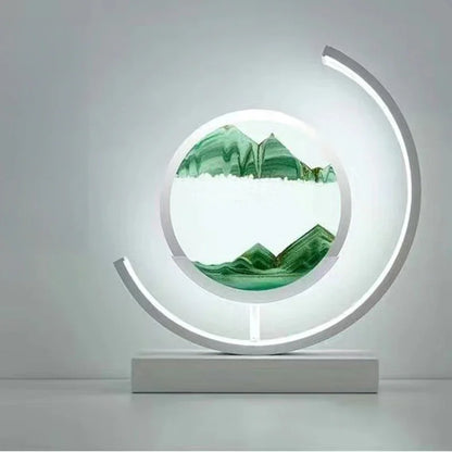Modern circular LED sand art lamp with green mountains design on a white base