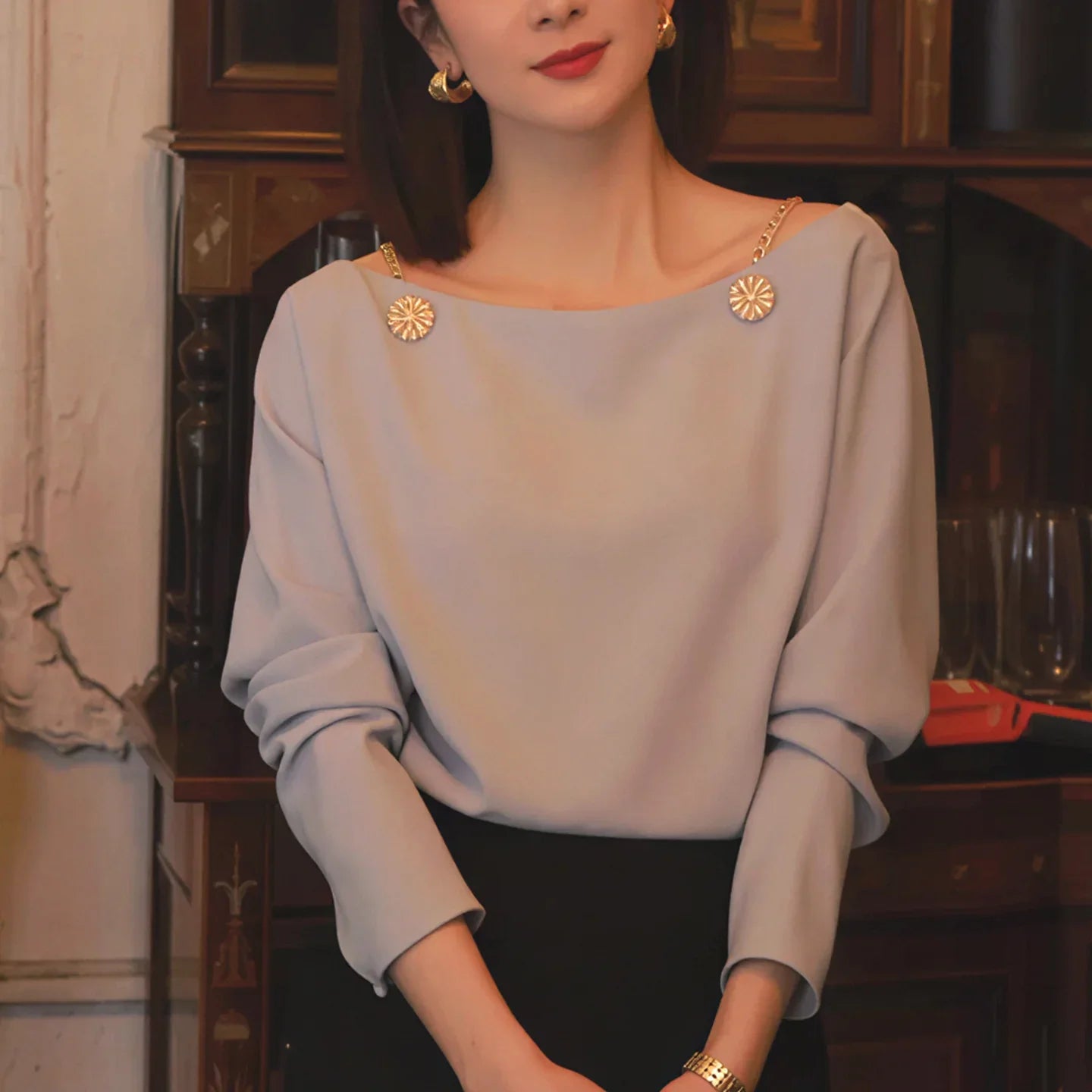 Woman in elegant pale blouse with gold chain accents and decorative buttons, gold earrings