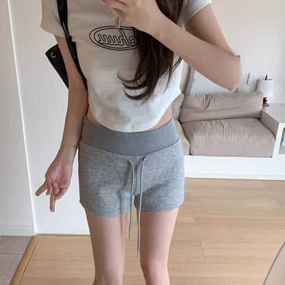 Person wearing a white t-shirt and gray shorts in a minimalistic room.