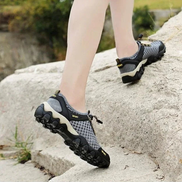 Person wearing black and gray mesh shoes on a rocky surface