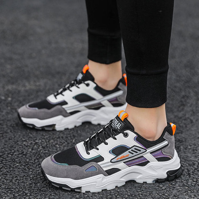 Gray and black sneakers with orange accents worn by a person on a dark surface.