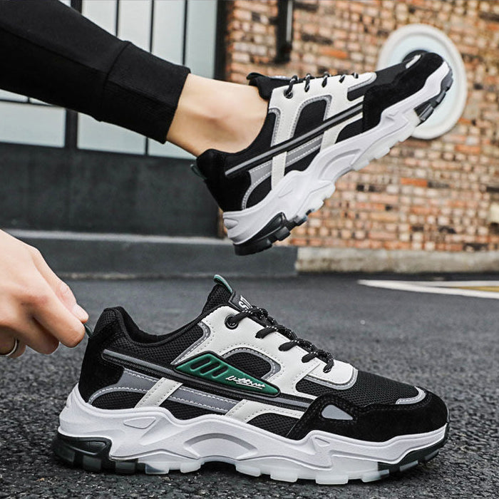 Black and white sneakers with green accents worn by a person on a street.