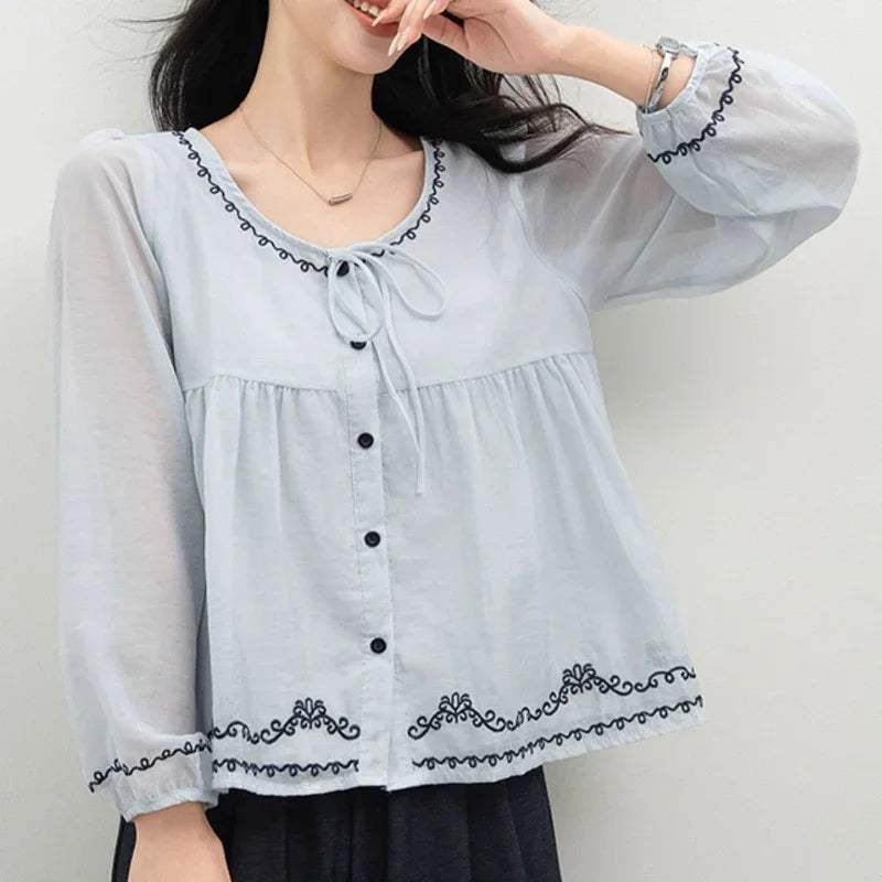 Light blue long sleeve embroidered blouse with black buttons and decorative trim.