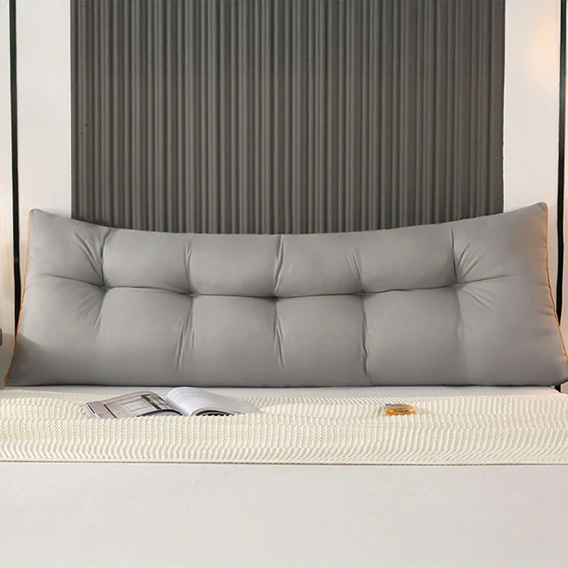 Modern bedroom with a large gray tufted backrest pillow on a bed, open magazine on blanket