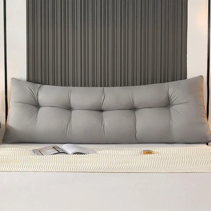 Modern bedroom with a large gray tufted backrest pillow on a bed, open magazine on blanket