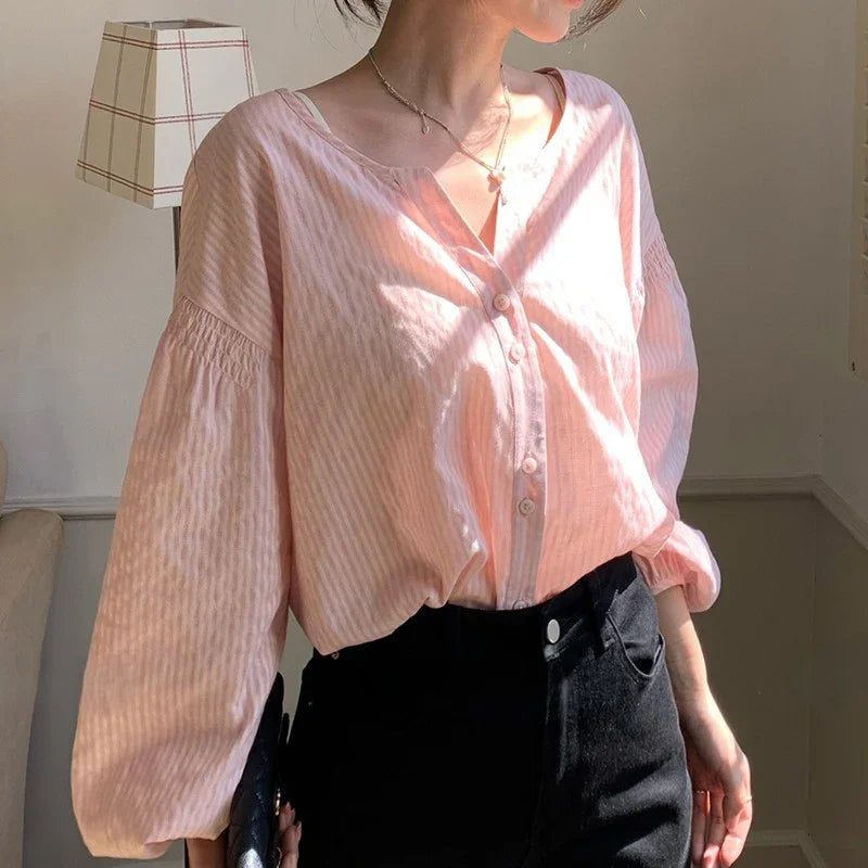 Woman wearing a light pink striped button-up blouse with black high-waisted pants