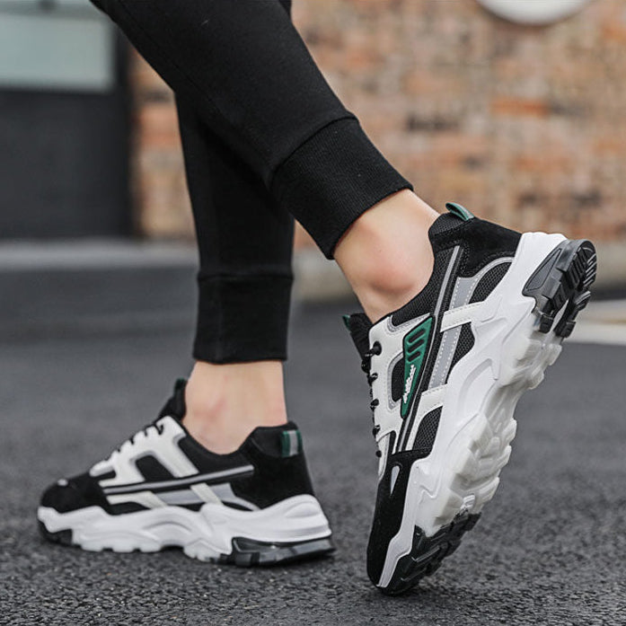 Person wearing black and white sneakers with green accents on a street.