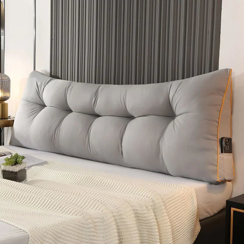 Modern bedroom with large gray tufted backrest pillow on bed, cozy knit blanket, and nightstand.