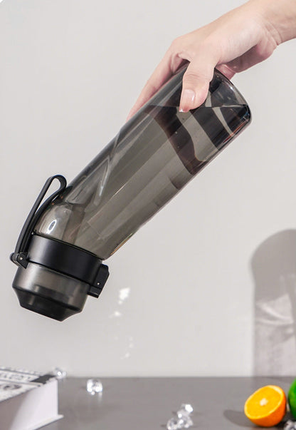 Hand holding a transparent travel water bottle with black lid on a light gray background.