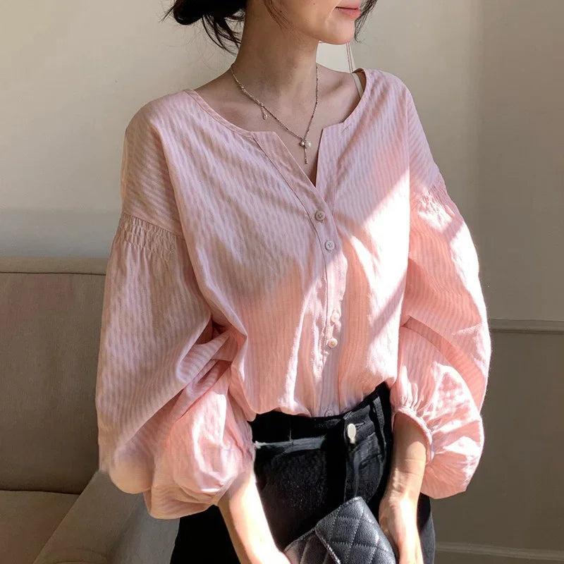 Woman wearing a light pink striped blouse with puffy sleeves and black pants