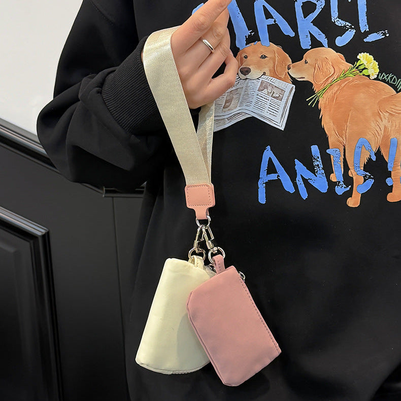 Person holding a small cream-colored handbag with a pink strap and matching pouch against a black sweatshirt with dog illustrations.