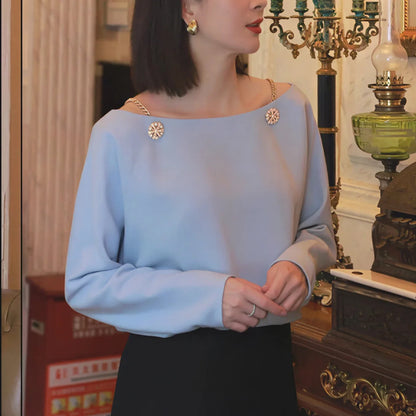 Woman wearing light blue long sleeve blouse with gold chain straps and decorative buttons