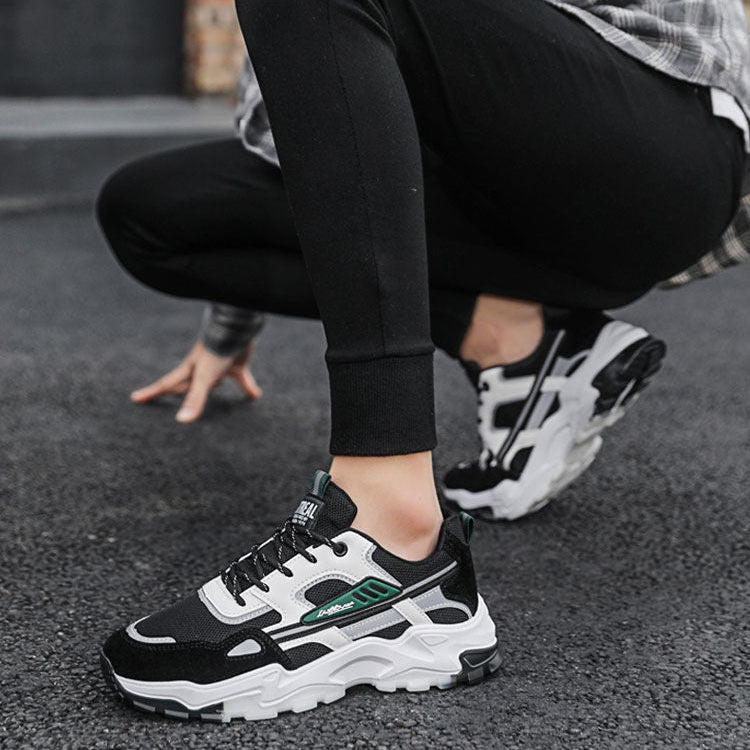 Person wearing black and white sneakers with green accents on a street.