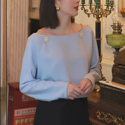 Woman in light blue chain-strap blouse with decorative buttons, elegant indoor setting