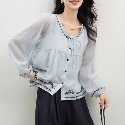 Woman wearing a light blue embroidered button-up blouse with sheer long sleeves