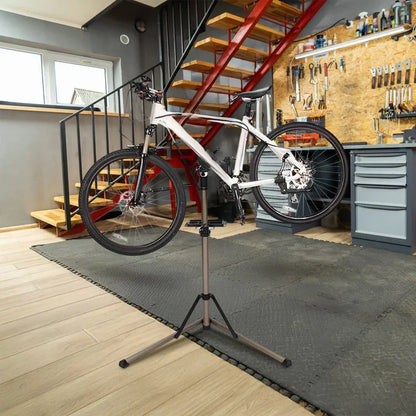 Mountain bike on repair stand in modern home workshop with tools and stairs in background