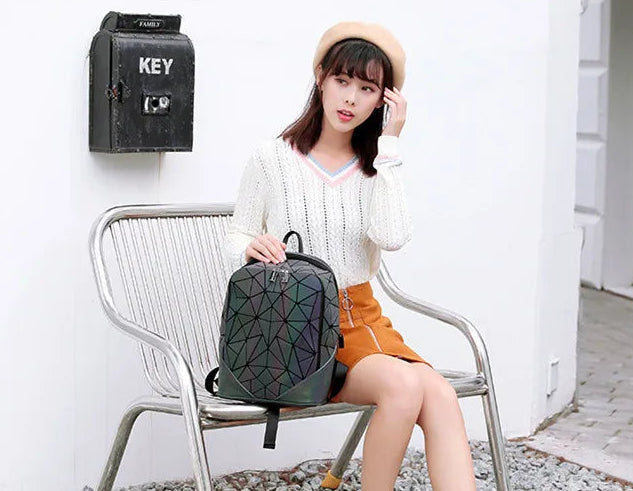 Woman sitting on a chair holding a geometric-patterned backpack against a white wall.