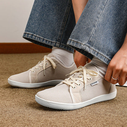 Beige sneakers worn with blue jeans on a carpeted floor.