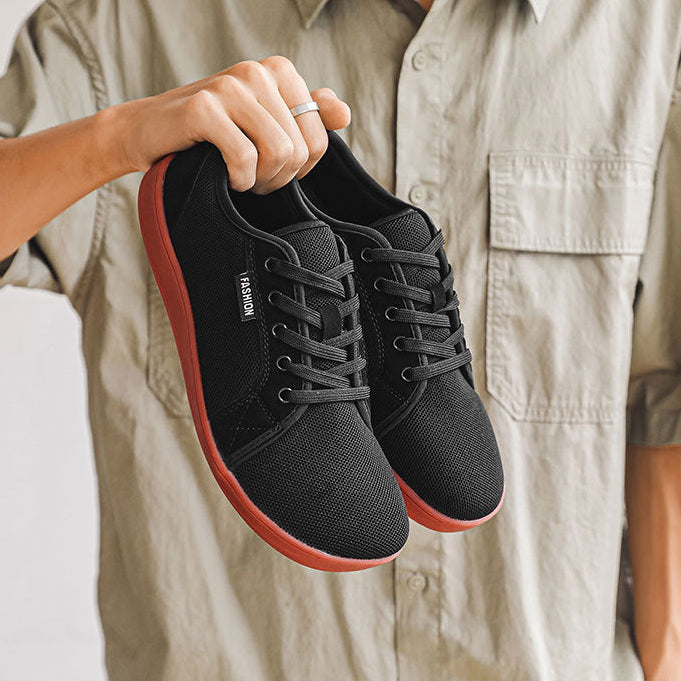 Person holding a pair of black sneakers with red soles